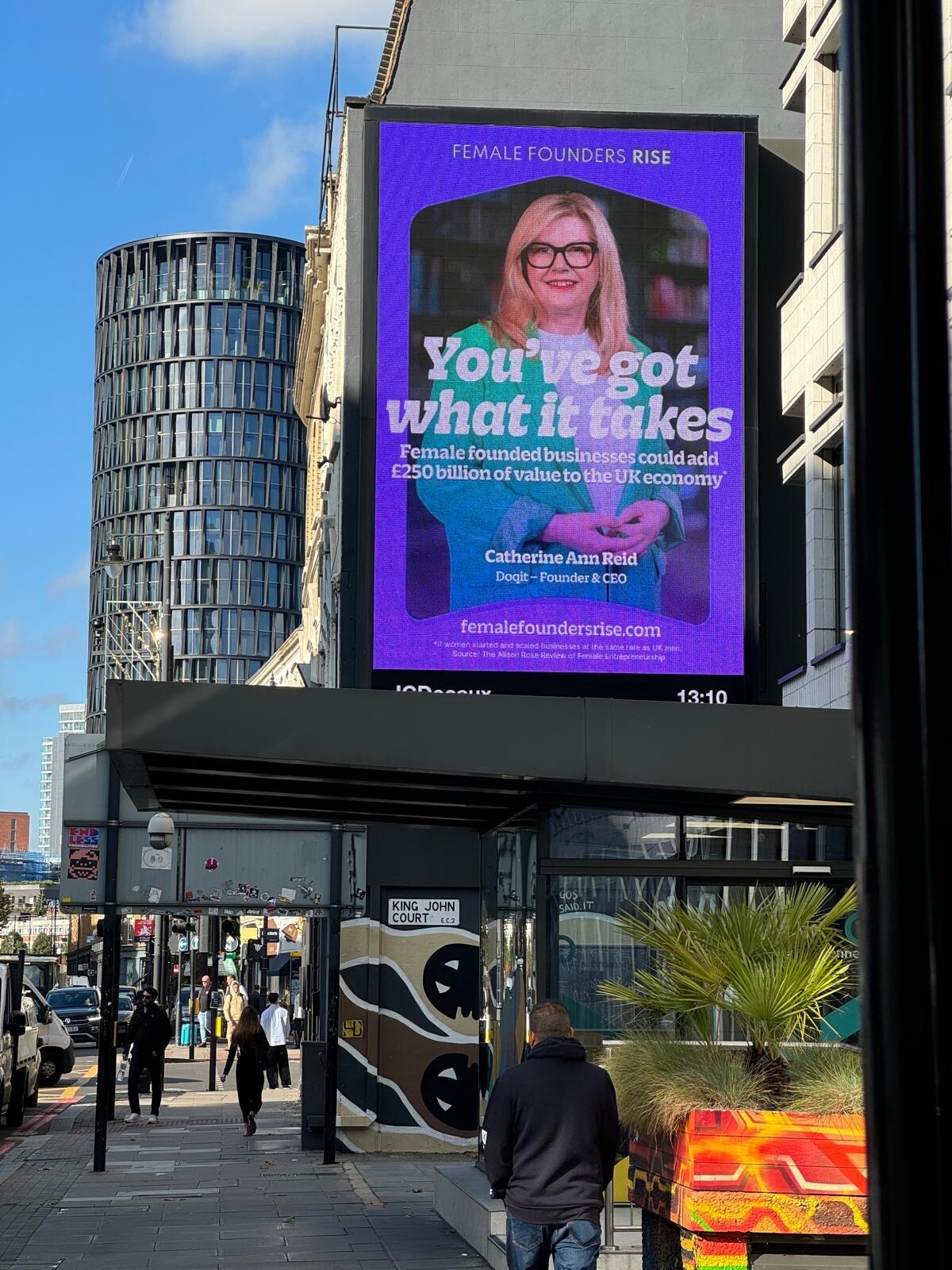 Image shows city scape  with billboard showing lady with light hair and green jacket.